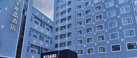 A modern hotel building with multiple floors, a prominent entrance with steps, and illuminated windows.