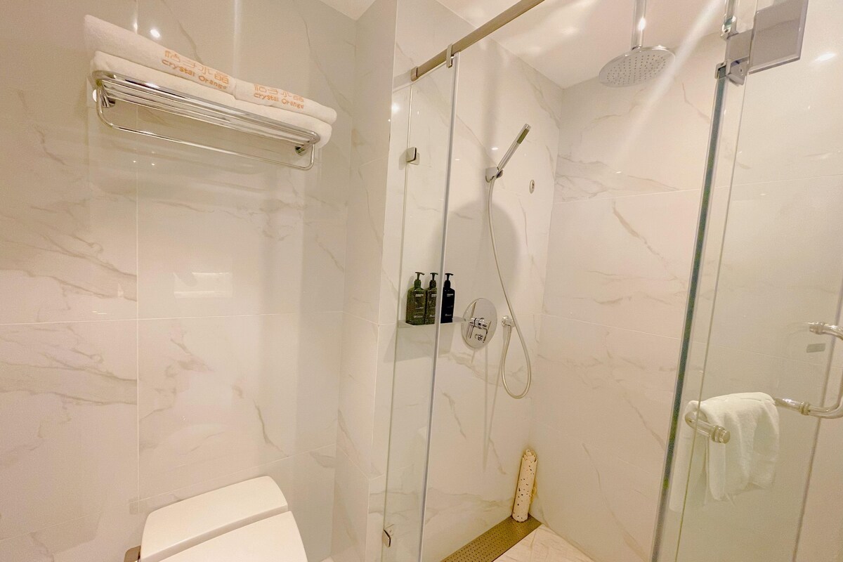 Un baño moderno con ducha envuelta en vidrio, inodoro y toallero con toallas.