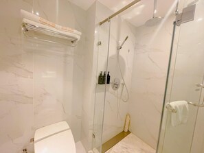 Un baño moderno con ducha envuelta en vidrio, inodoro y toallero con toallas.