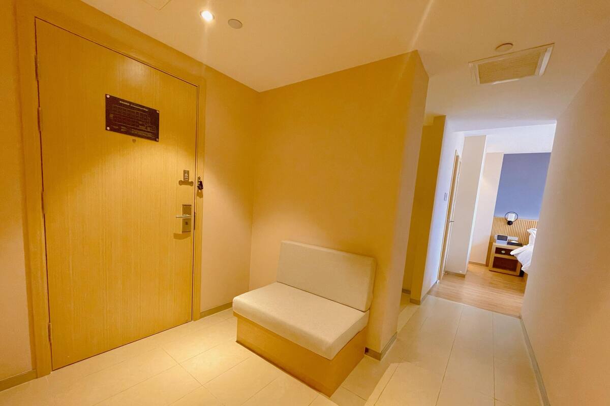Un pasillo de hotel con una puerta de madera, un banco y una cama al fondo.