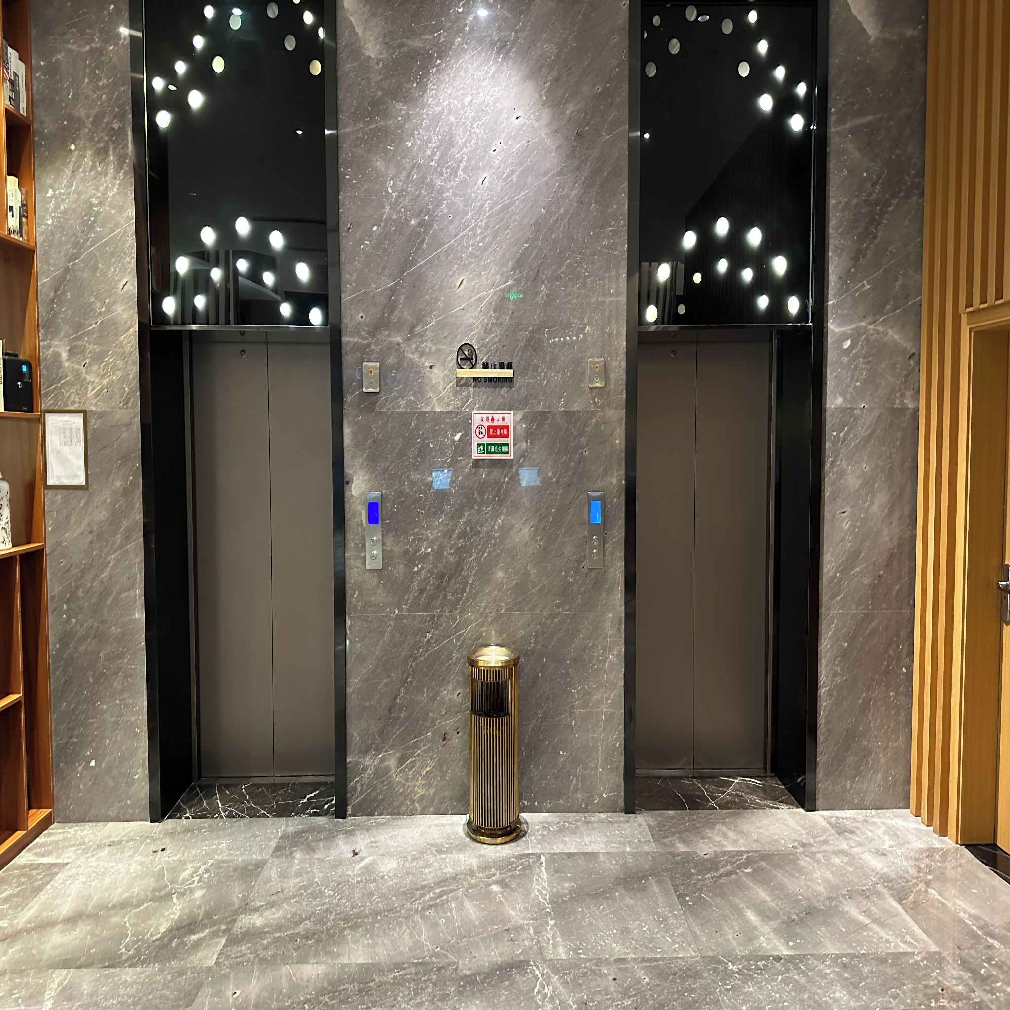 A modern elevator with a marble wall and a trash can in the center.