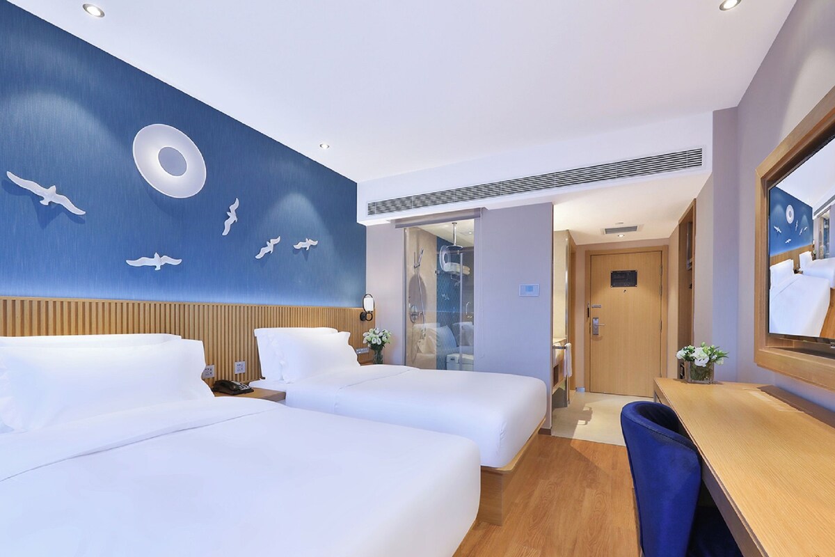 Habitación de hotel con dos camas, un escritorio y un espejo grande.