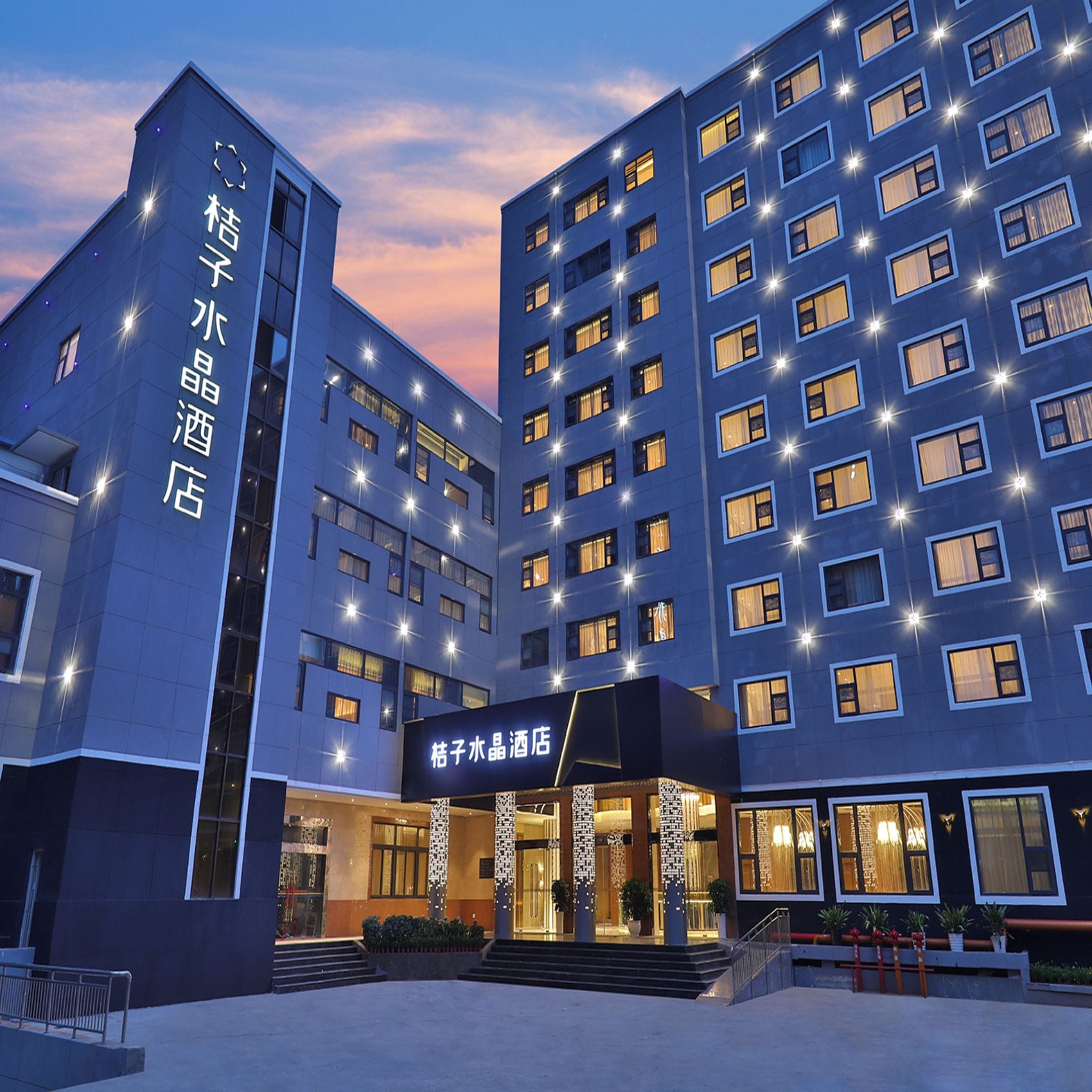 A modern hotel building with multiple floors, illuminated windows, and a prominent entrance with a sign.