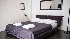Ein ordentlich gemachtes Bett mit einer dunkel gemusterten Tagesdecke, weißen Kissen und gefalteten Handtüchern.
