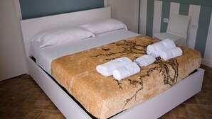 Una cama bien hecha con una colcha floral y dos toallas enrolladas a un lado.