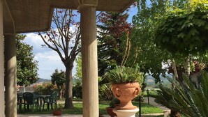 Un espacio al aire libre techado con una estructura de pérgola, plantas en macetas y vistas del paisaje circundante.