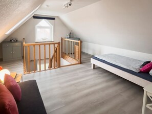 Un dormitorio tipo loft con techo inclinado, una cama, un escritorio y una ventana.