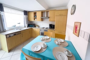 Cocina compacta con armarios de madera, microondas, estufa y una mesa de comedor con platos y tazas.