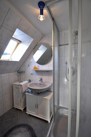 Une salle de bain moderne avec un puits de lumière, un grand miroir, un lavabo et une douche.
