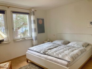 Une chambre à coucher avec un lit, une fenêtre avec un rideau, une lampe fixée au mur et un tableau encadré.