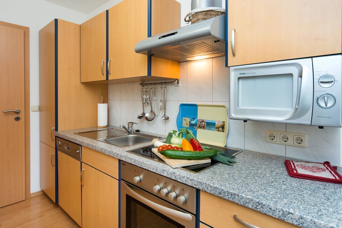A compact kitchen with wooden cabinets, a stainless steel sink, a microwave, and a stove.