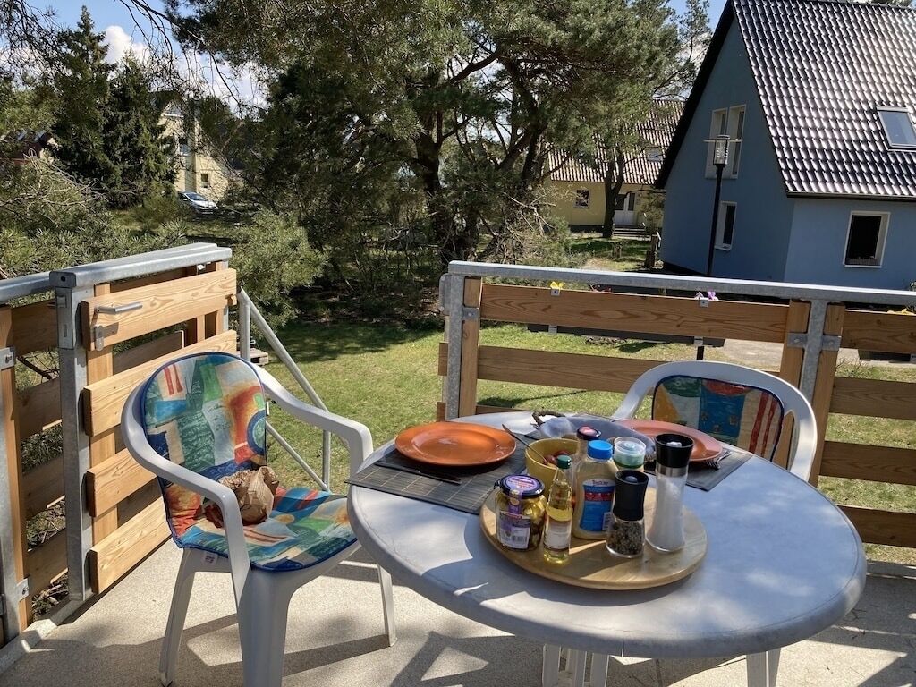 An outdoor dining area with a round table and two chairs, a wooden fence, and a house in the background.