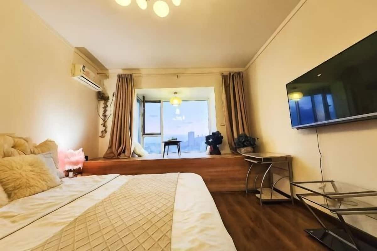 A bedroom with a bed, a TV, a desk, and a window with curtains.