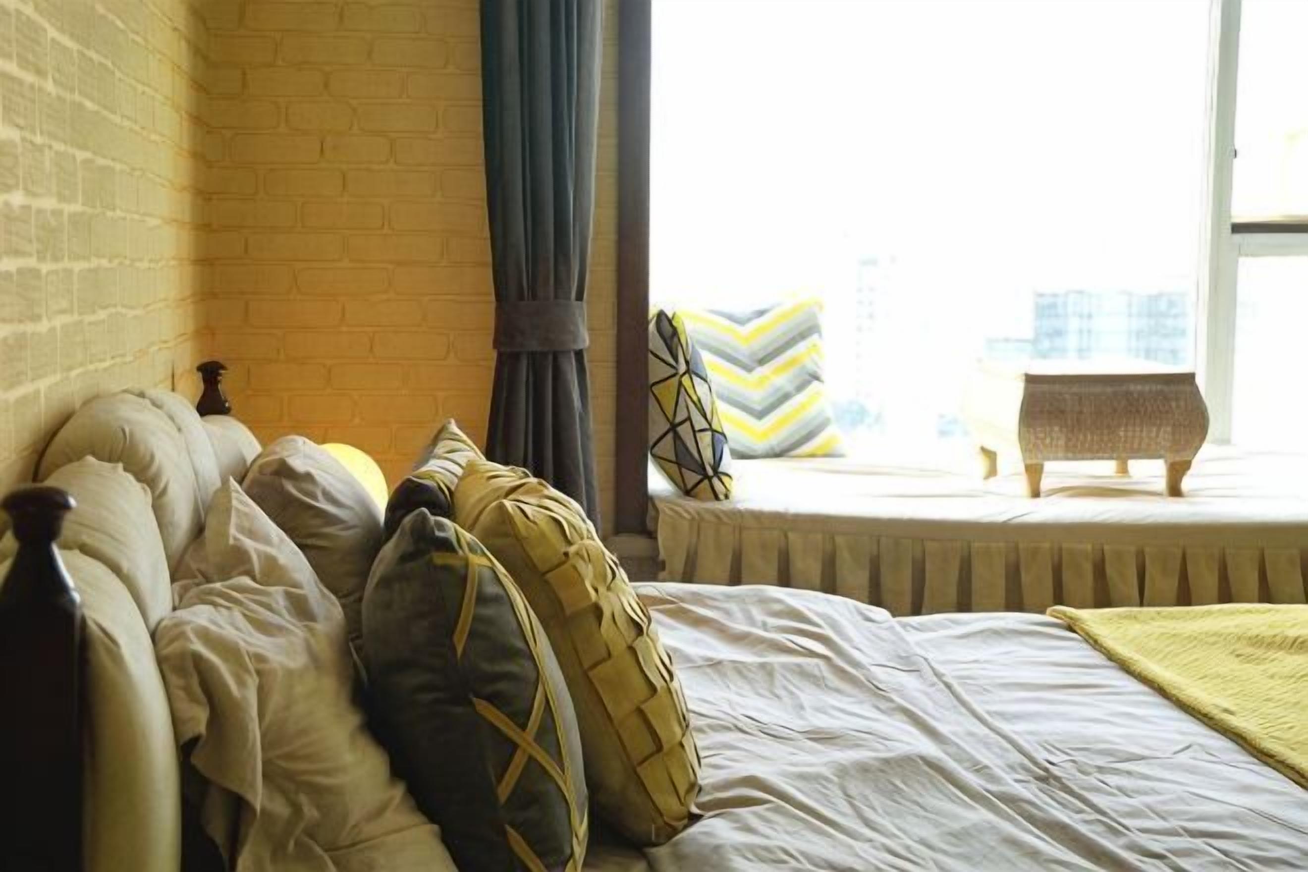 A bed with pillows, a window with curtains, and a view of buildings.