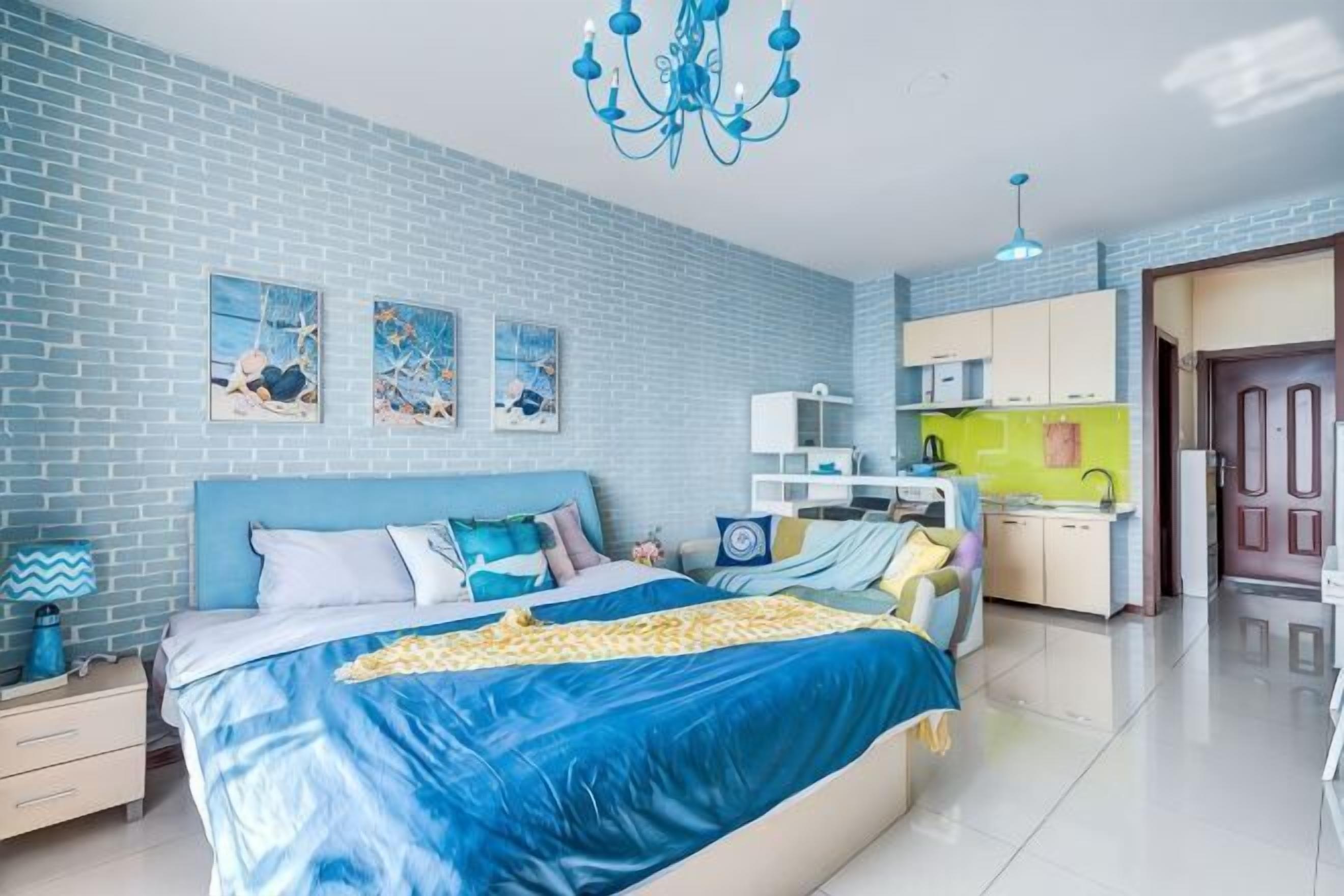 A bedroom with a bed, a nightstand, a dresser, a desk, and a kitchenette.