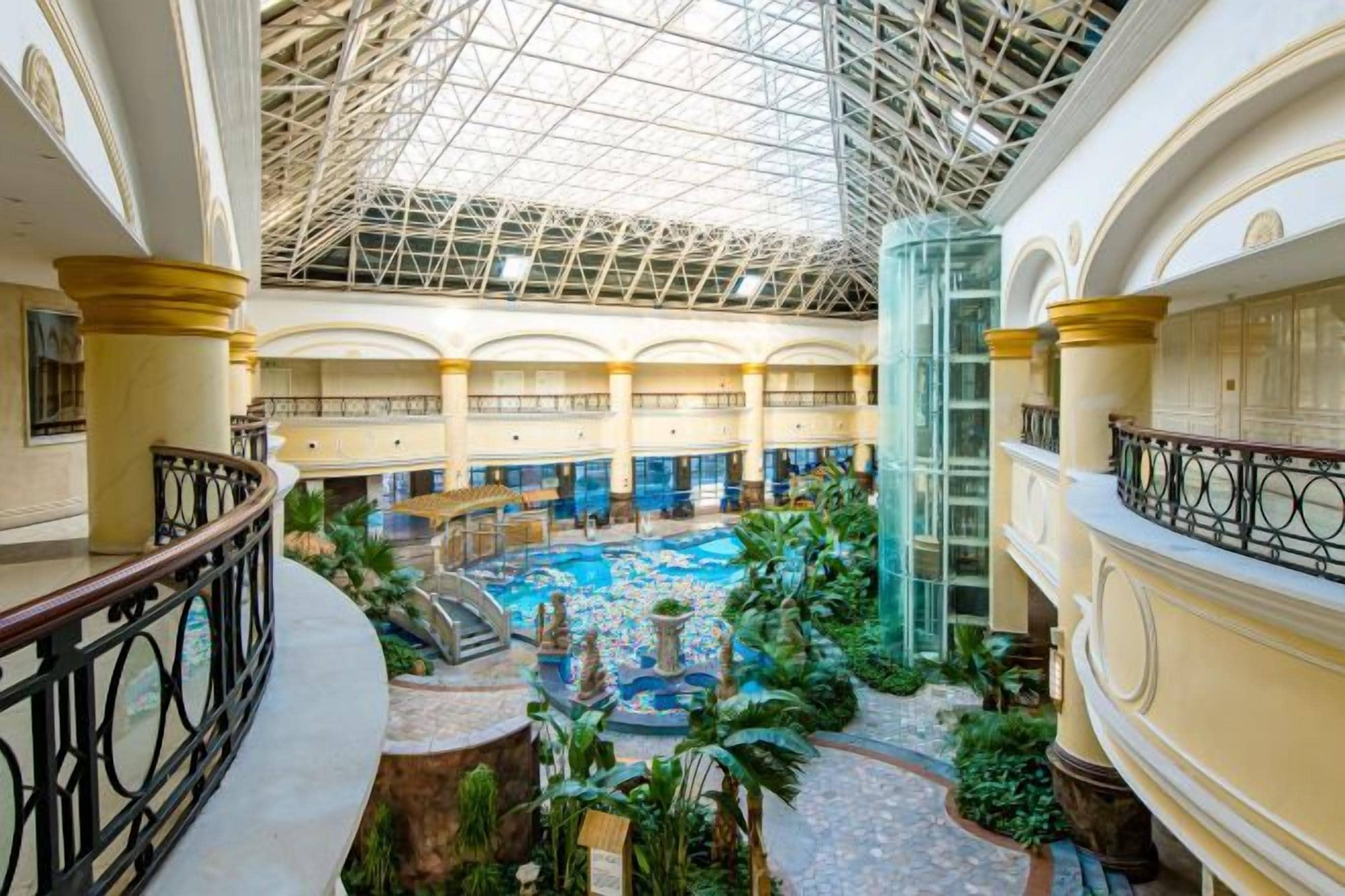 A spacious atrium with a central pool, multiple balconies, and a glass ceiling.
