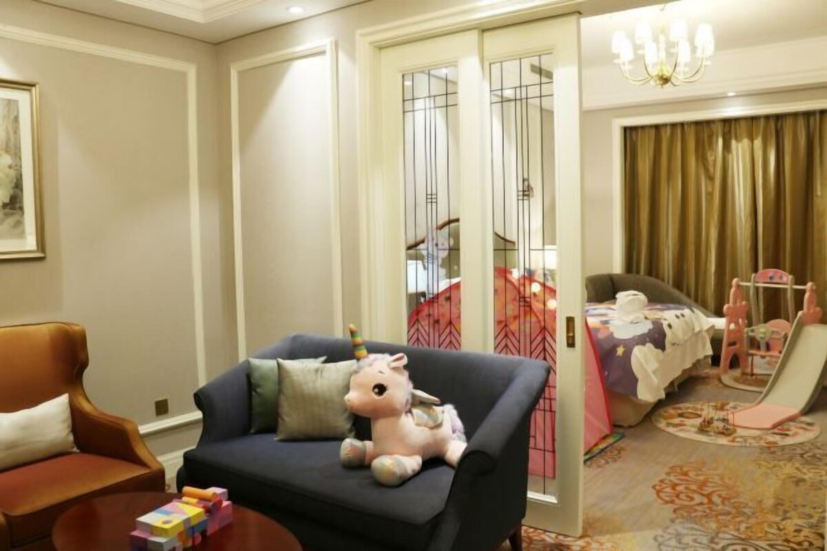 A hotel room with a sofa, a small table with toys, a bed with a pink canopy, and a chandelier.