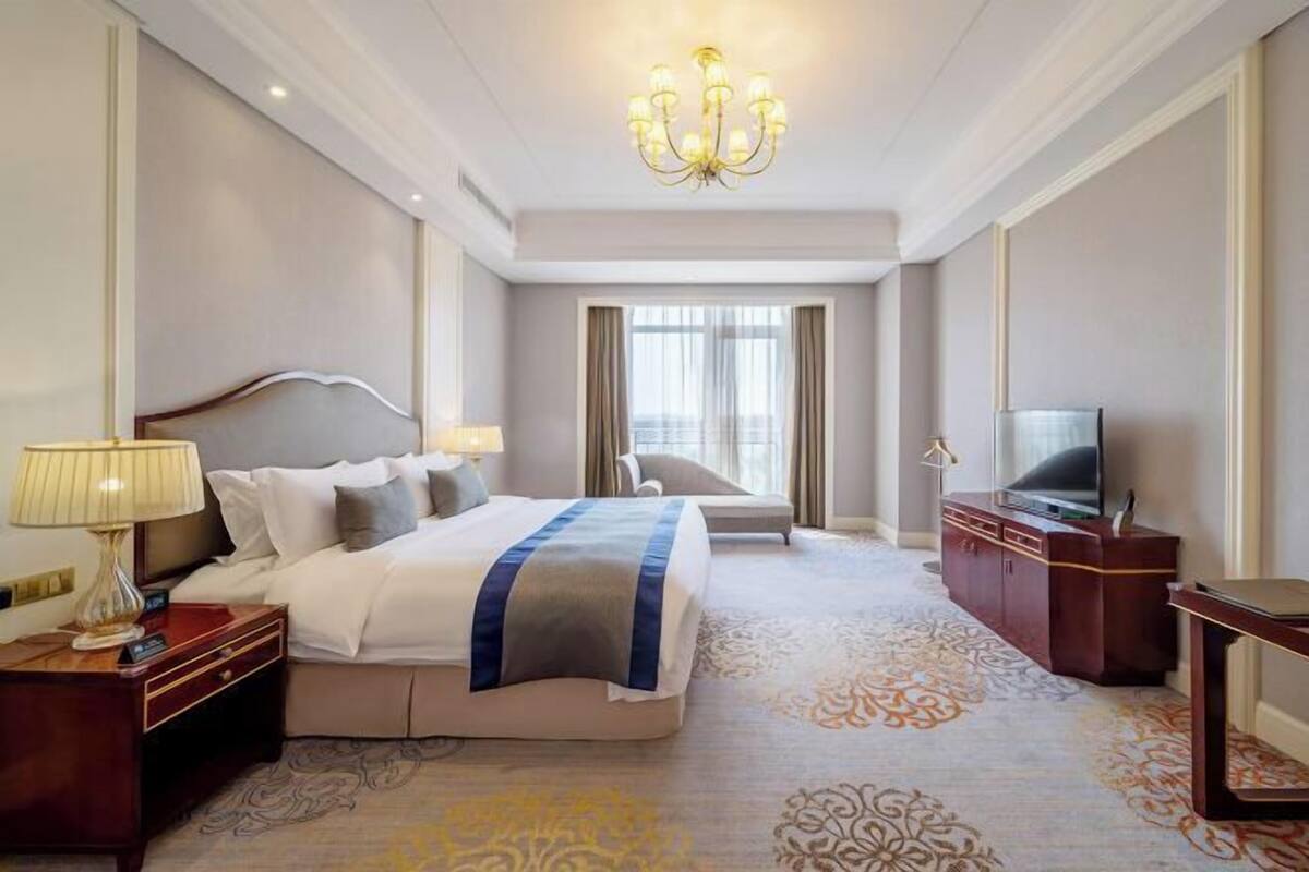 A hotel room with a large bed, a television, a desk, and a chandelier.