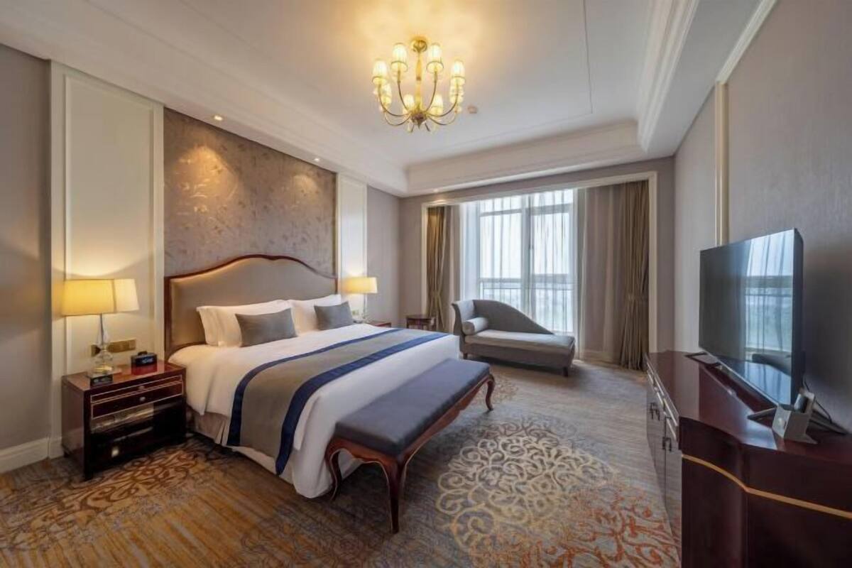 A hotel room with a large bed, a desk, a television, and a view of the outdoors.