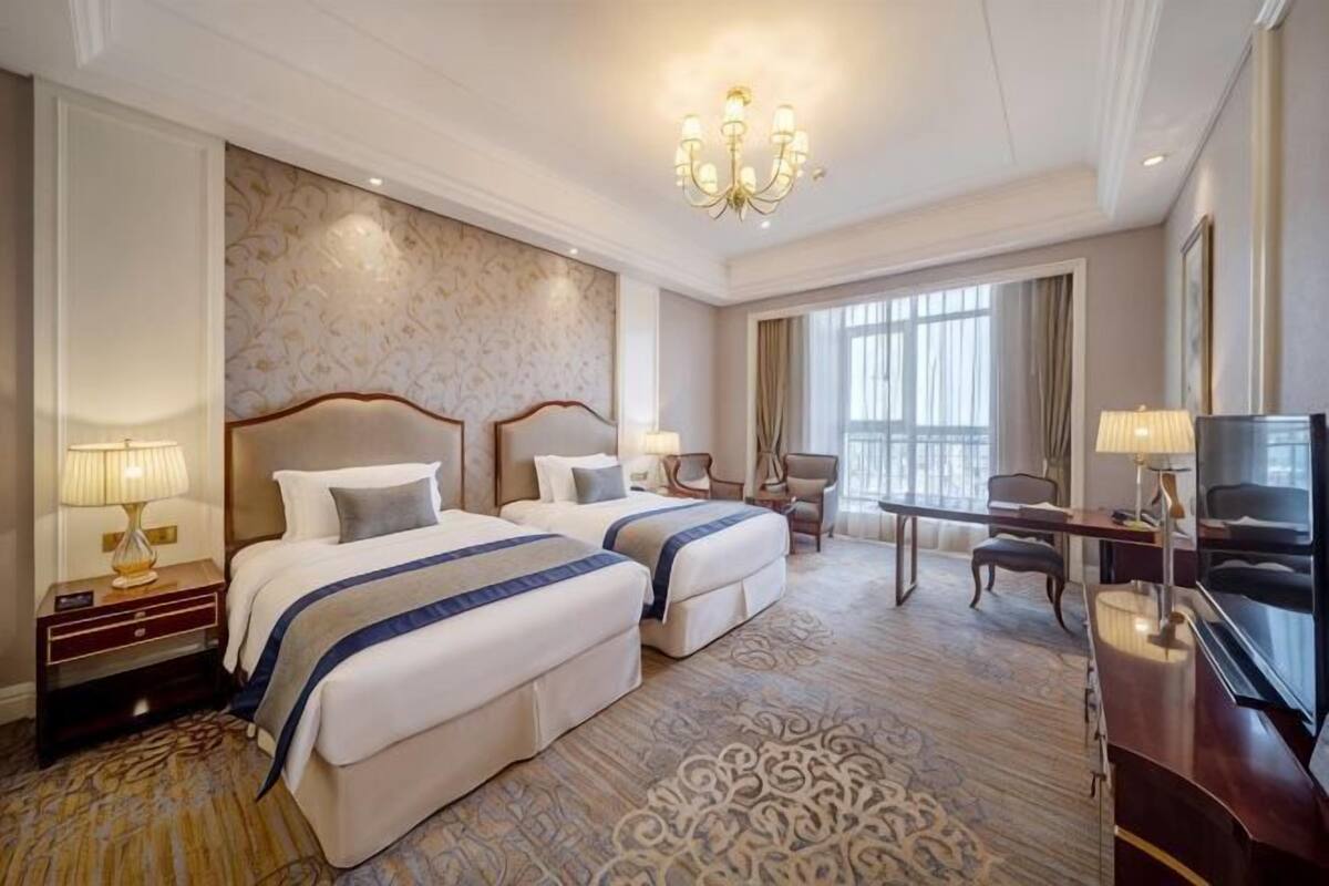 A hotel room with two beds, a desk, a TV, and a large window.