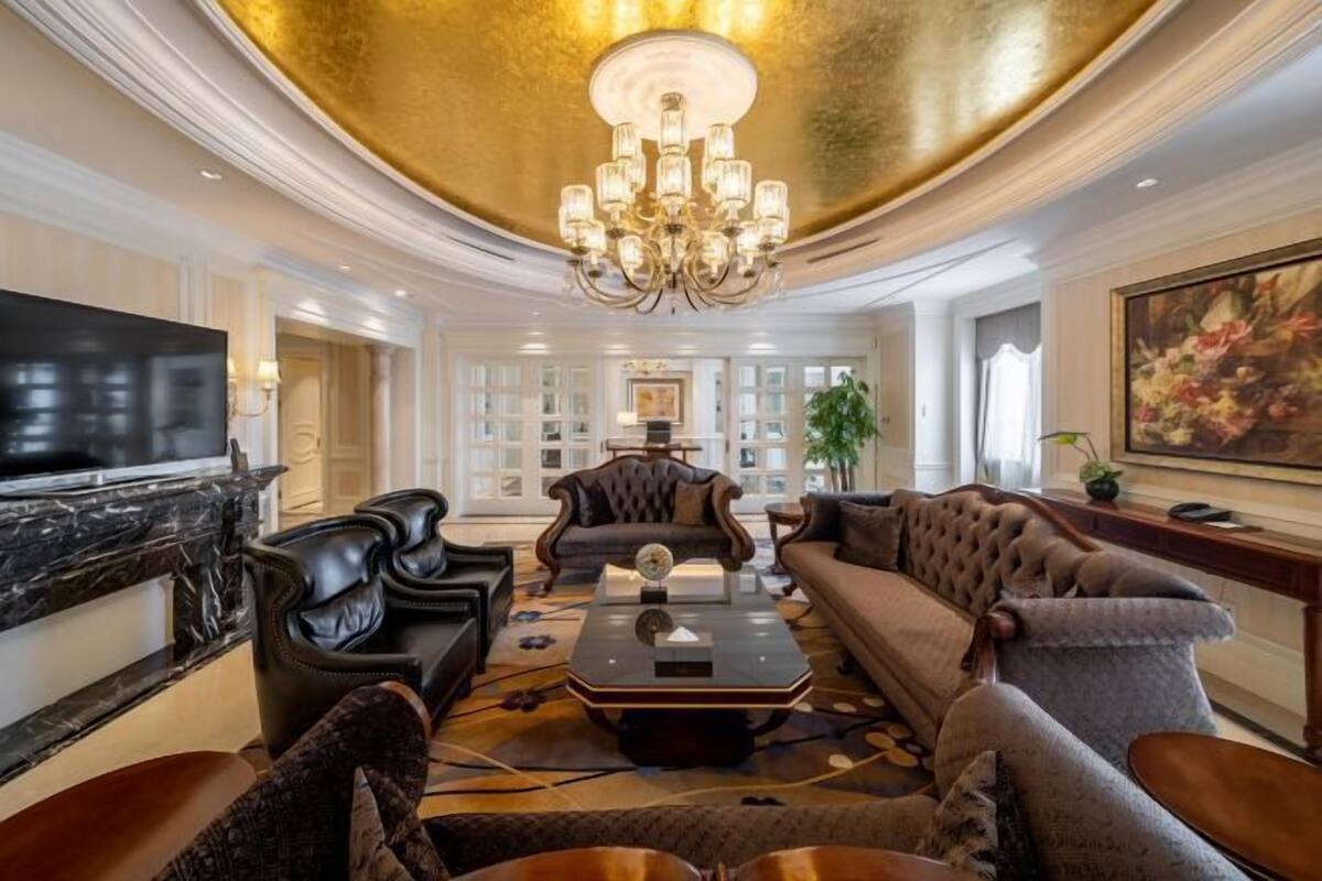 A luxurious living room with a chandelier, leather sofas, a flat-screen TV, and a marble fireplace.