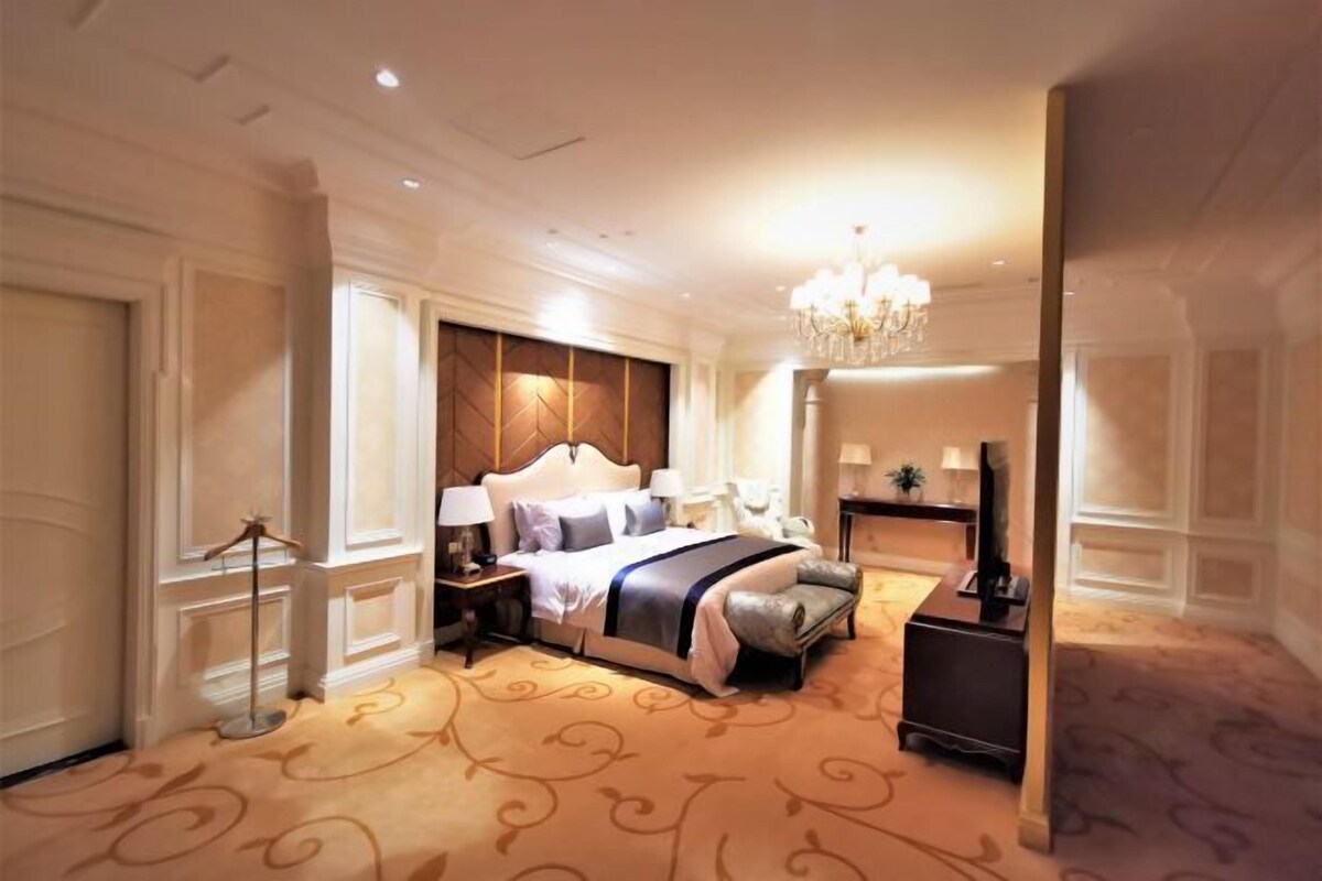 A spacious hotel room with a large bed, a chandelier, a desk, and a chair.