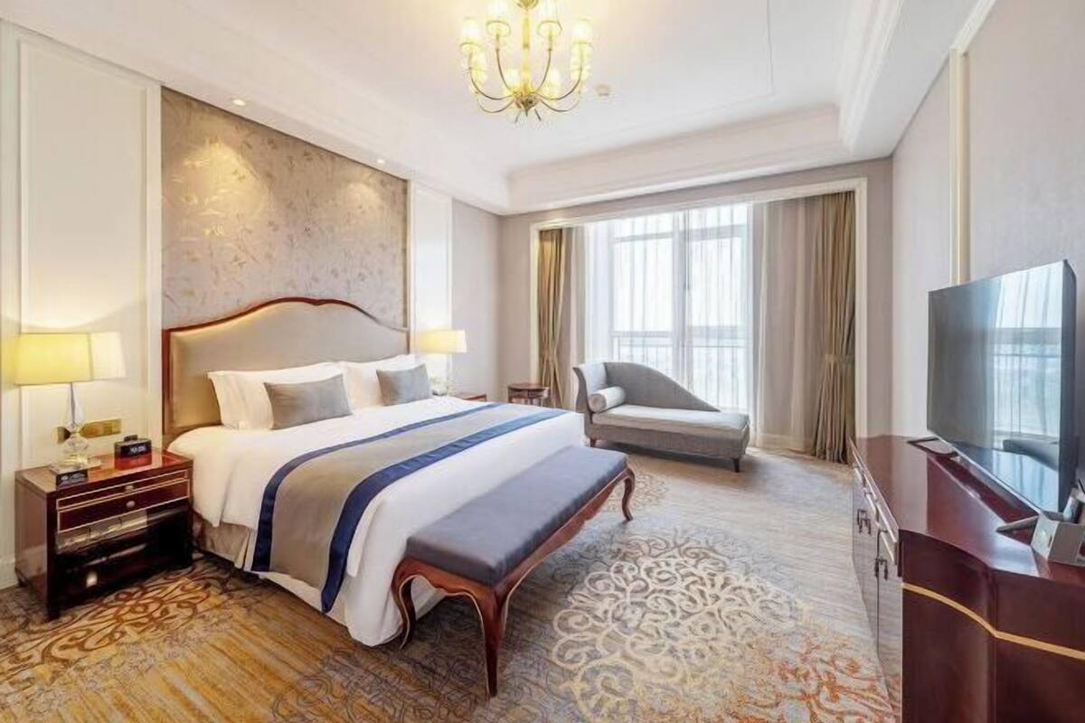 A hotel room with a large bed, a desk, a television, and a chandelier.