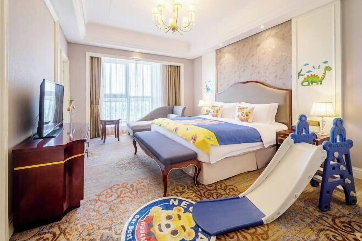 A hotel room with a bed, a desk, a TV, a desk lamp, a chair, a window, and a slide.