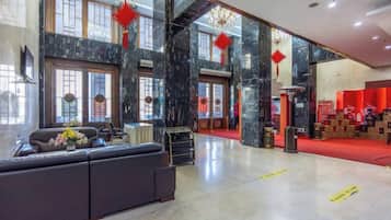 A spacious lobby with a seating area, large windows, and a red carpet leading to a reception desk.