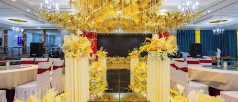 Un salón de banquetes con mesas redondas, sillas blancas y un pasillo central.
