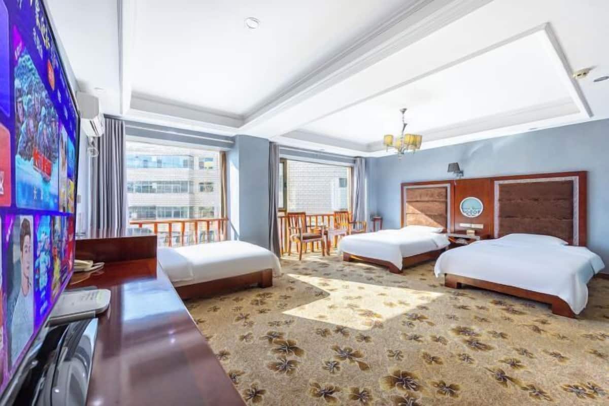 A hotel room with two beds, a desk, a TV, and a balcony.