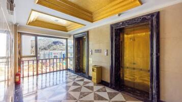A hotel lobby with a checkered floor, a balcony with a railing, and a large elevator with a gold finish.