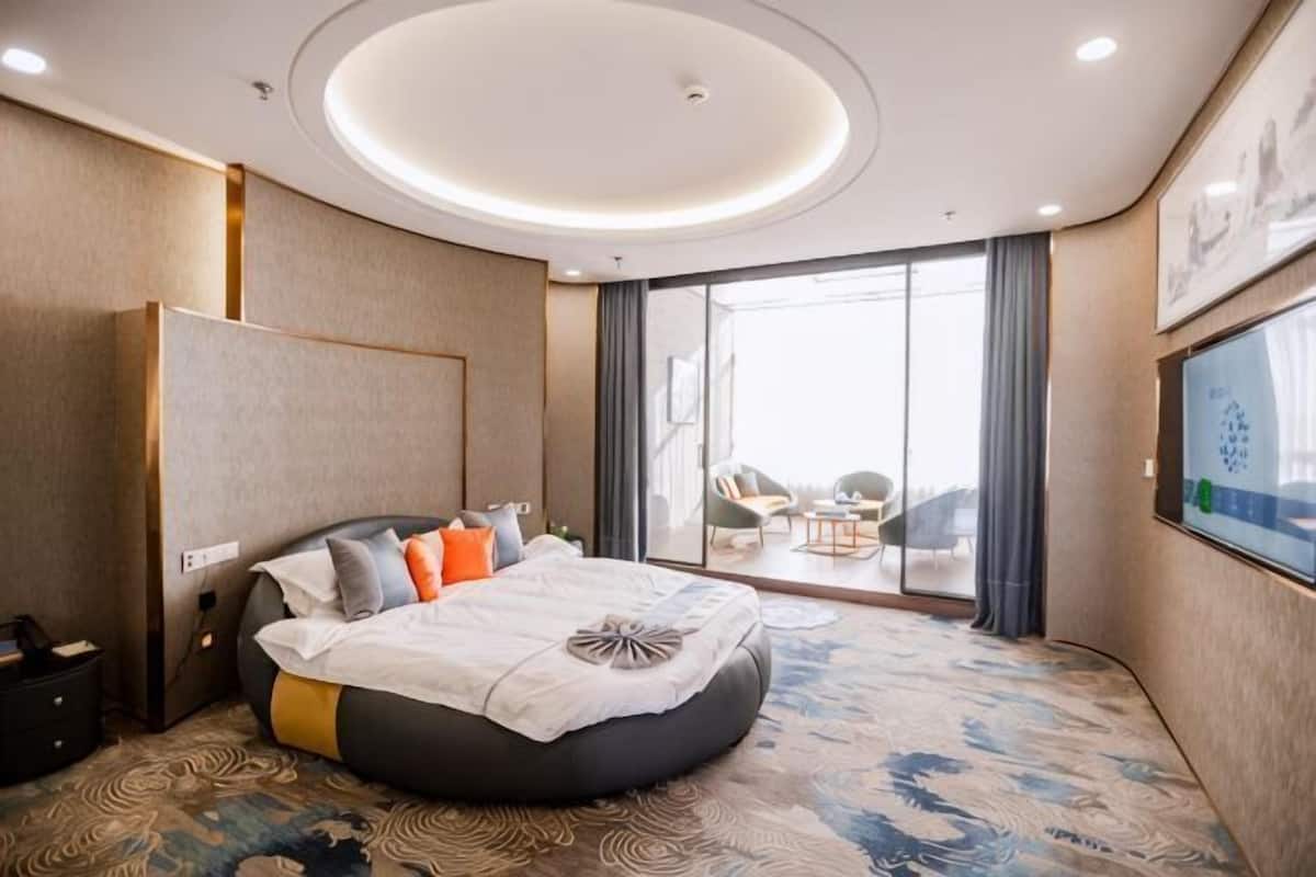 Una habitación de hotel moderna con una cama grande, vistas al exterior y un balcón con mobiliario.