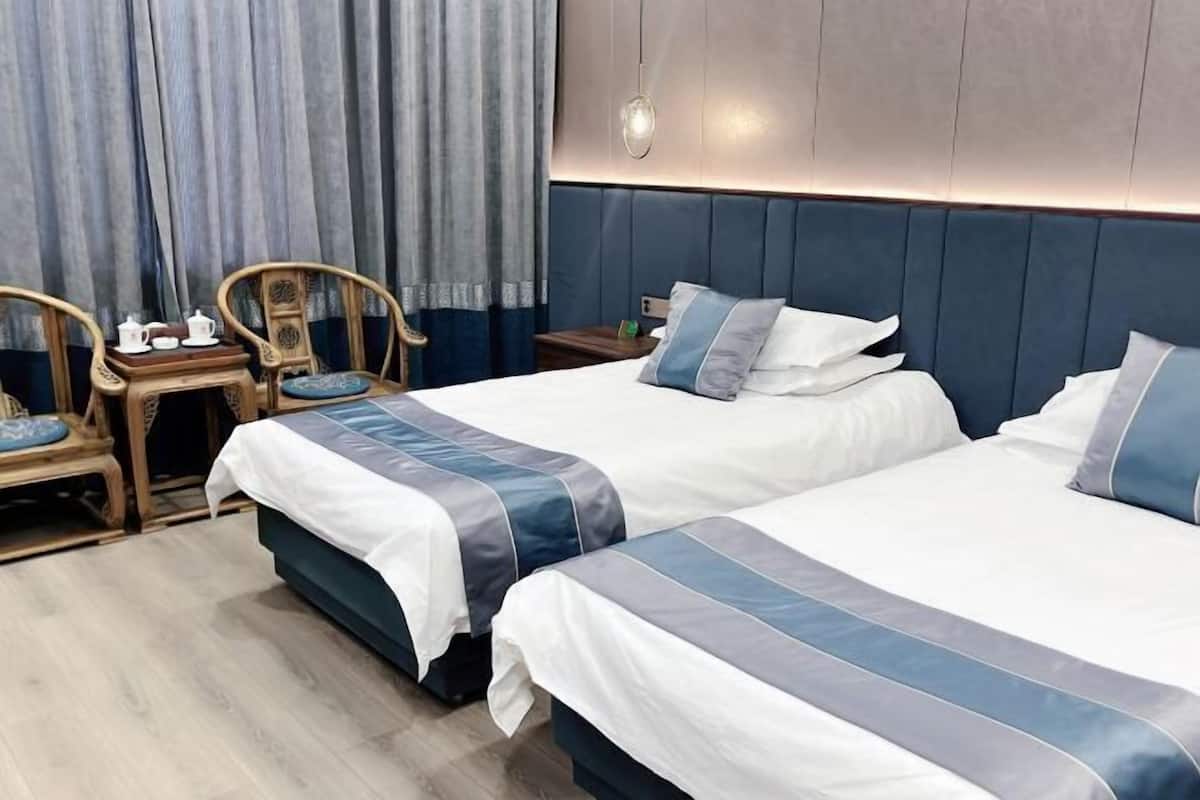 Habitación de hotel con dos camas, una mesita con juego de té y una silla.