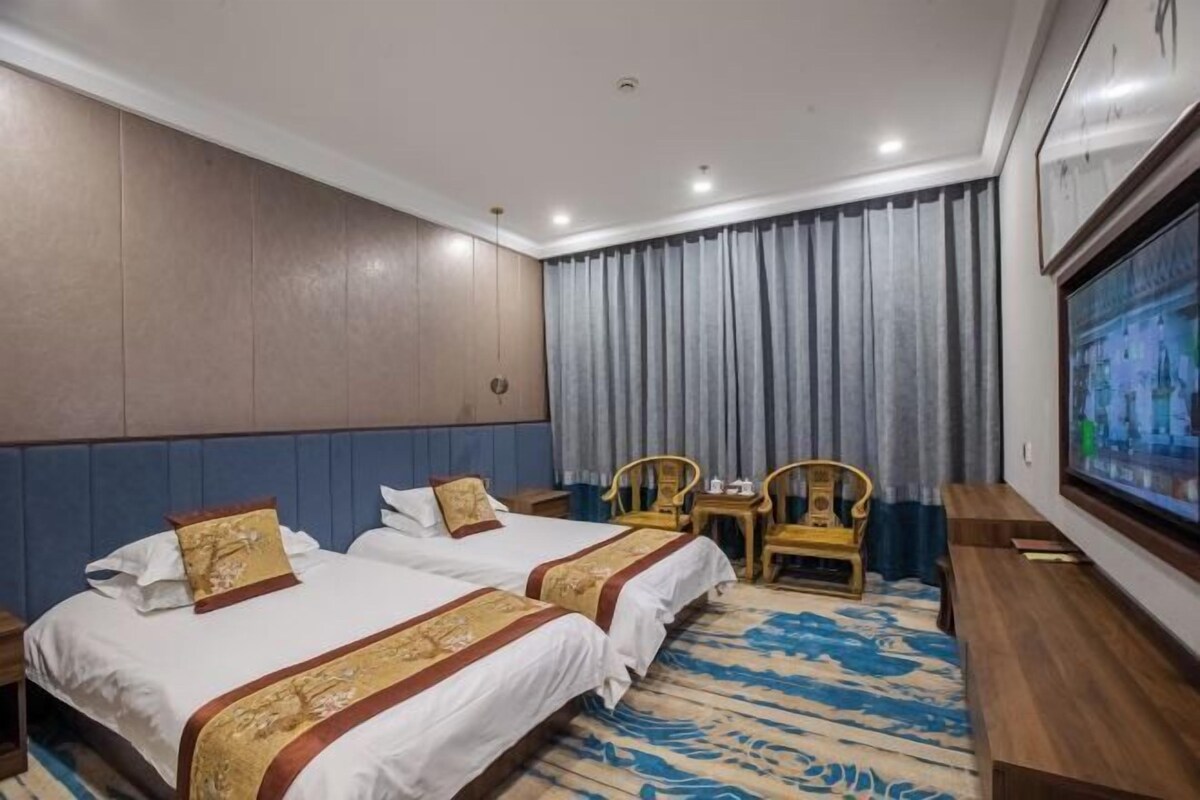 A hotel room with two beds, a television, a desk, and a chair.