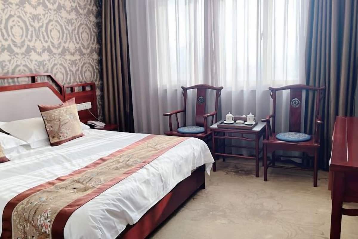 Habitación de hotel con cama, dos sillas de madera, una mesita y una ventana con cortinas.