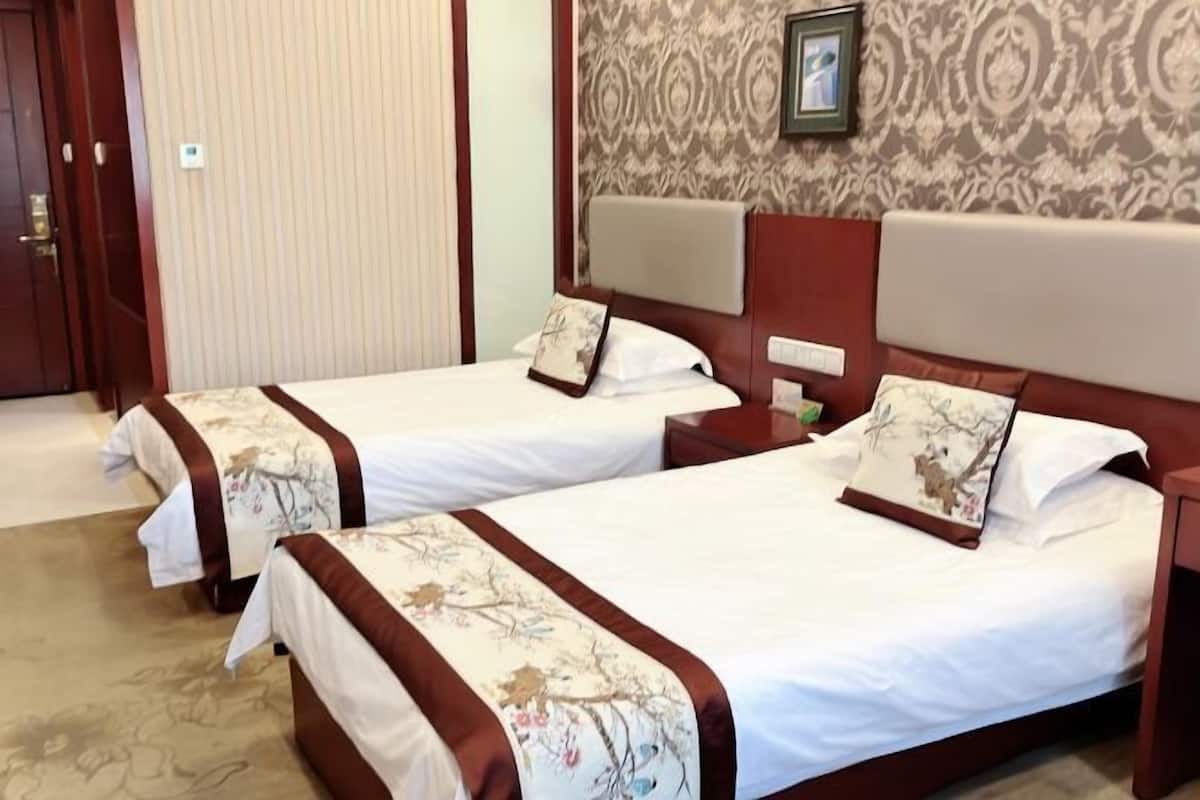 Habitación de hotel con dos camas, cada una con cabecera, mesitas de noche y mesillas.