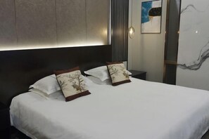 A neatly made bed with white linens and two decorative pillows, a modern headboard, and a marble wall with a painting. - Villa Lido (Laiyang)