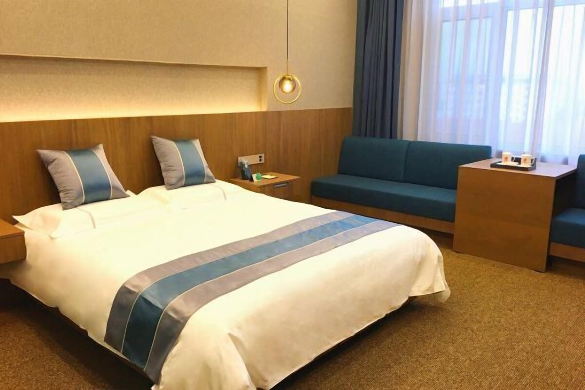 A hotel room with a large bed, a sofa, a nightstand, and a lamp.