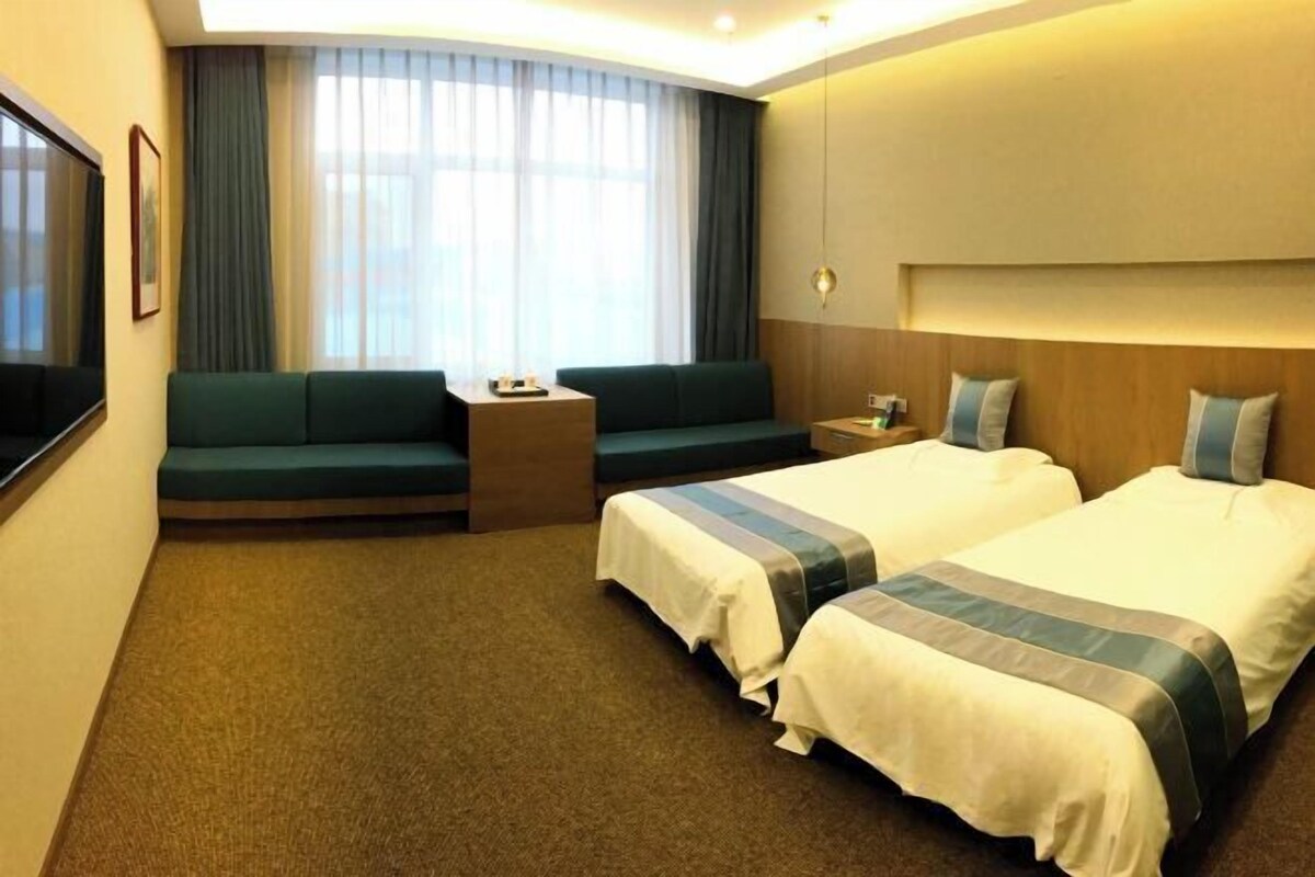 A hotel room with two beds, a sofa, a TV, and a window with curtains.