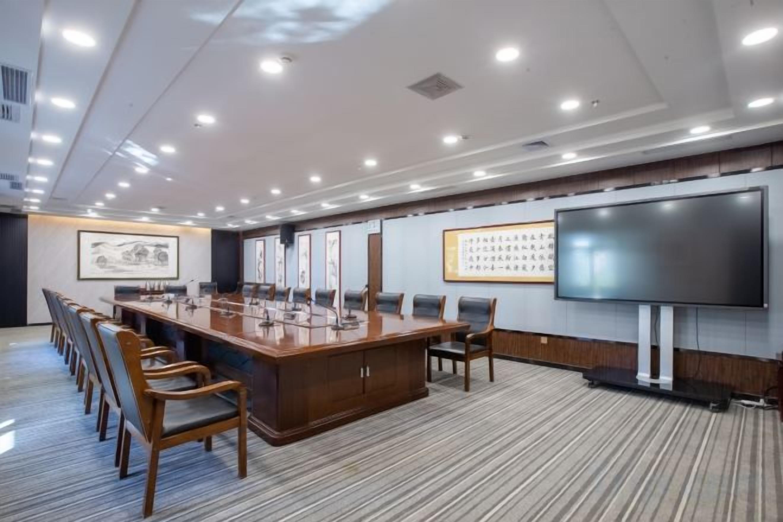 Un salón de conferencias con una larga mesa, sillas, una pantalla grande y cuadros en las paredes.