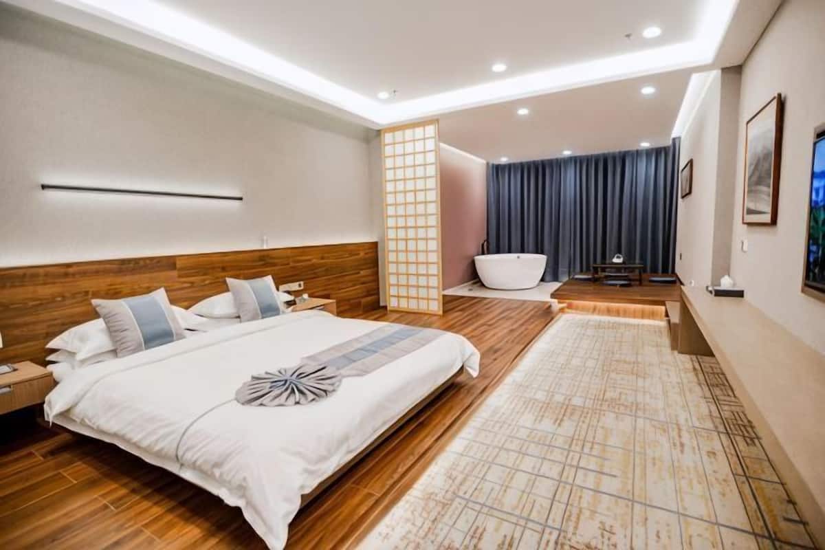 Una habitación de hotel moderna con una cama grande, una bañera y piso de madera.