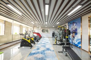 A gym with exercise equipment, a blue patterned floor, and a large window on the left. - Villa Lido (Laiyang)