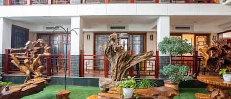 A multi-level indoor space with wooden furniture and plants, featuring a balcony with a railing.