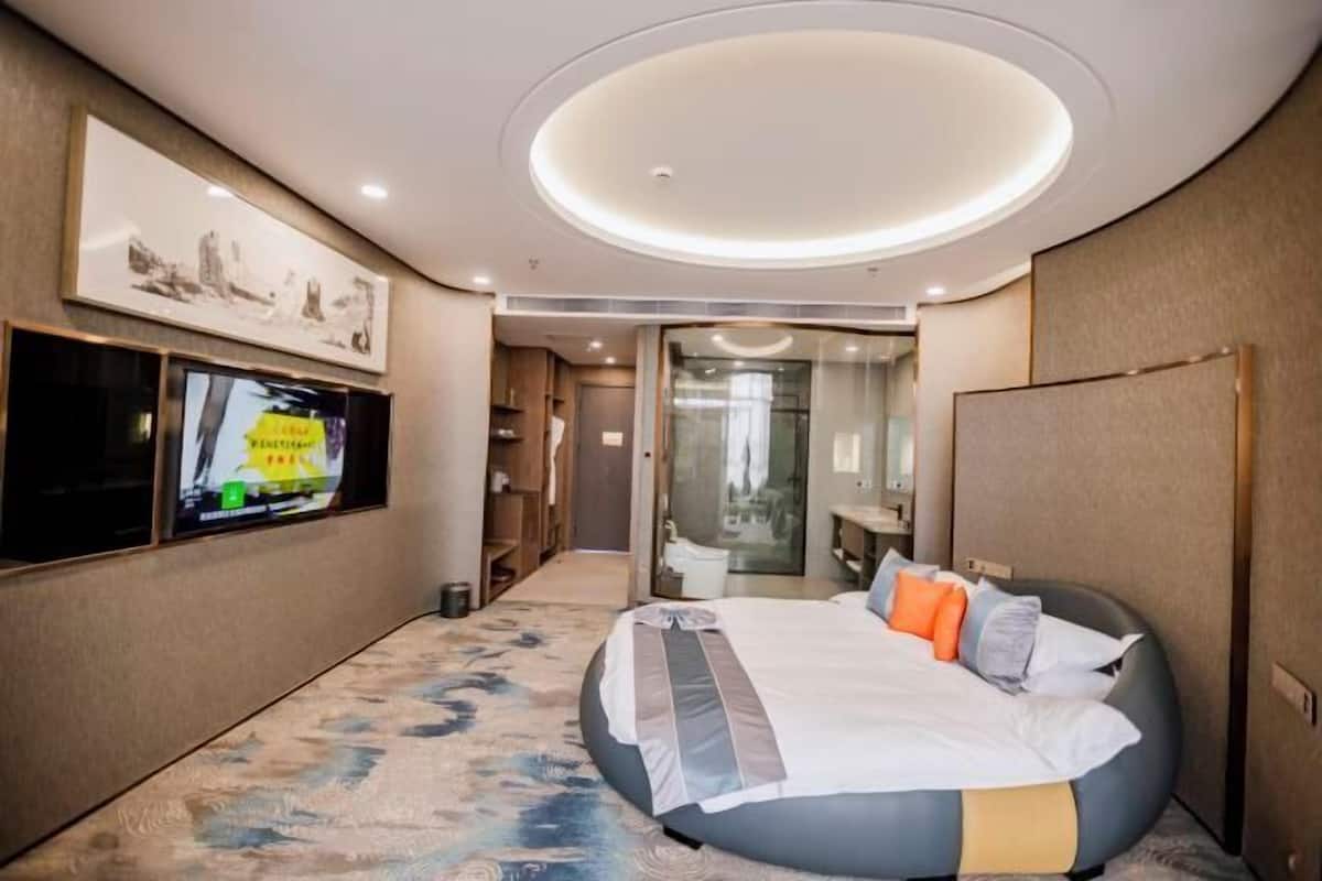 Una habitación de hotel moderna con una cama grande, un televisor montado en la pared y una lámpara de techo circular.