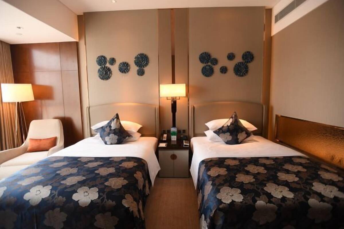 A hotel room with two beds, a nightstand, a lamp, and decorative wall art.