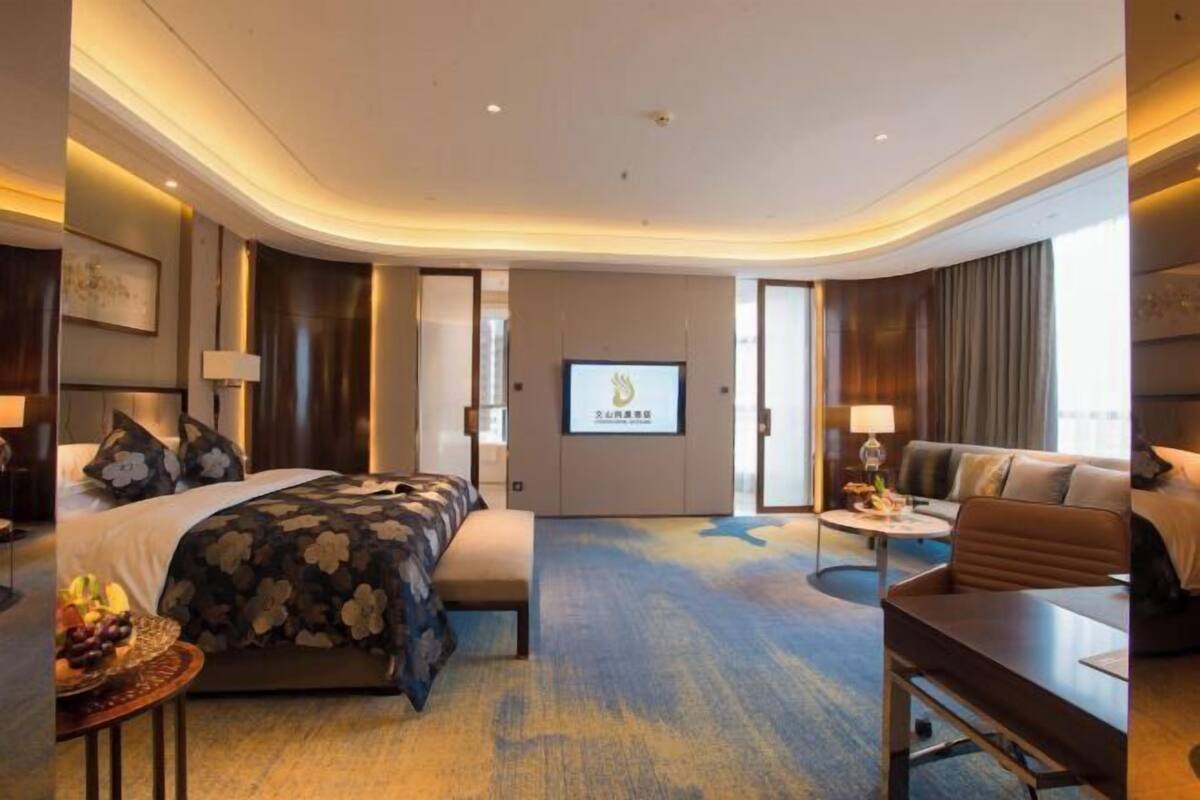 A modern hotel room with a bed, a sofa, a desk, and a TV.