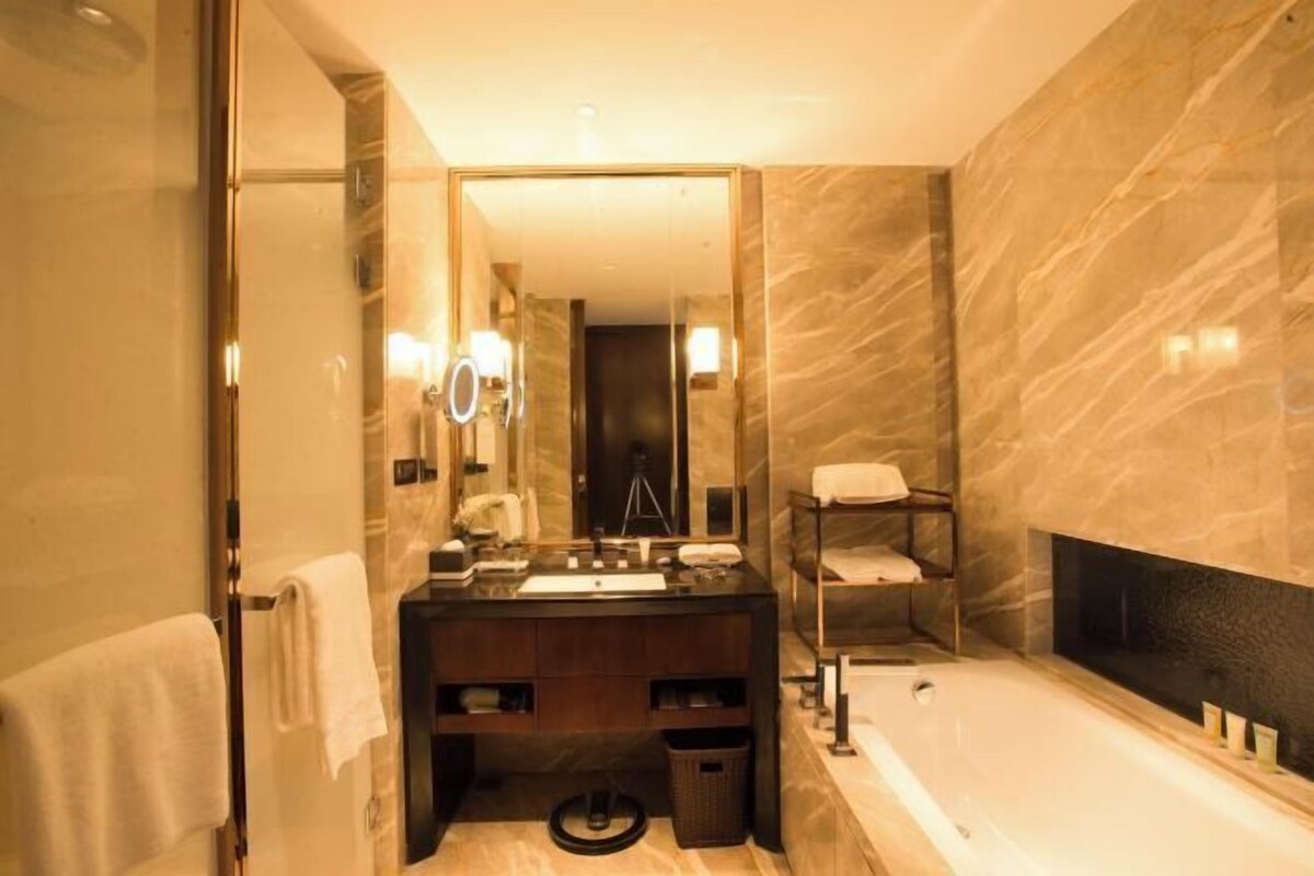 A modern bathroom with a large mirror, a bathtub, a vanity with a sink, and a towel rack.