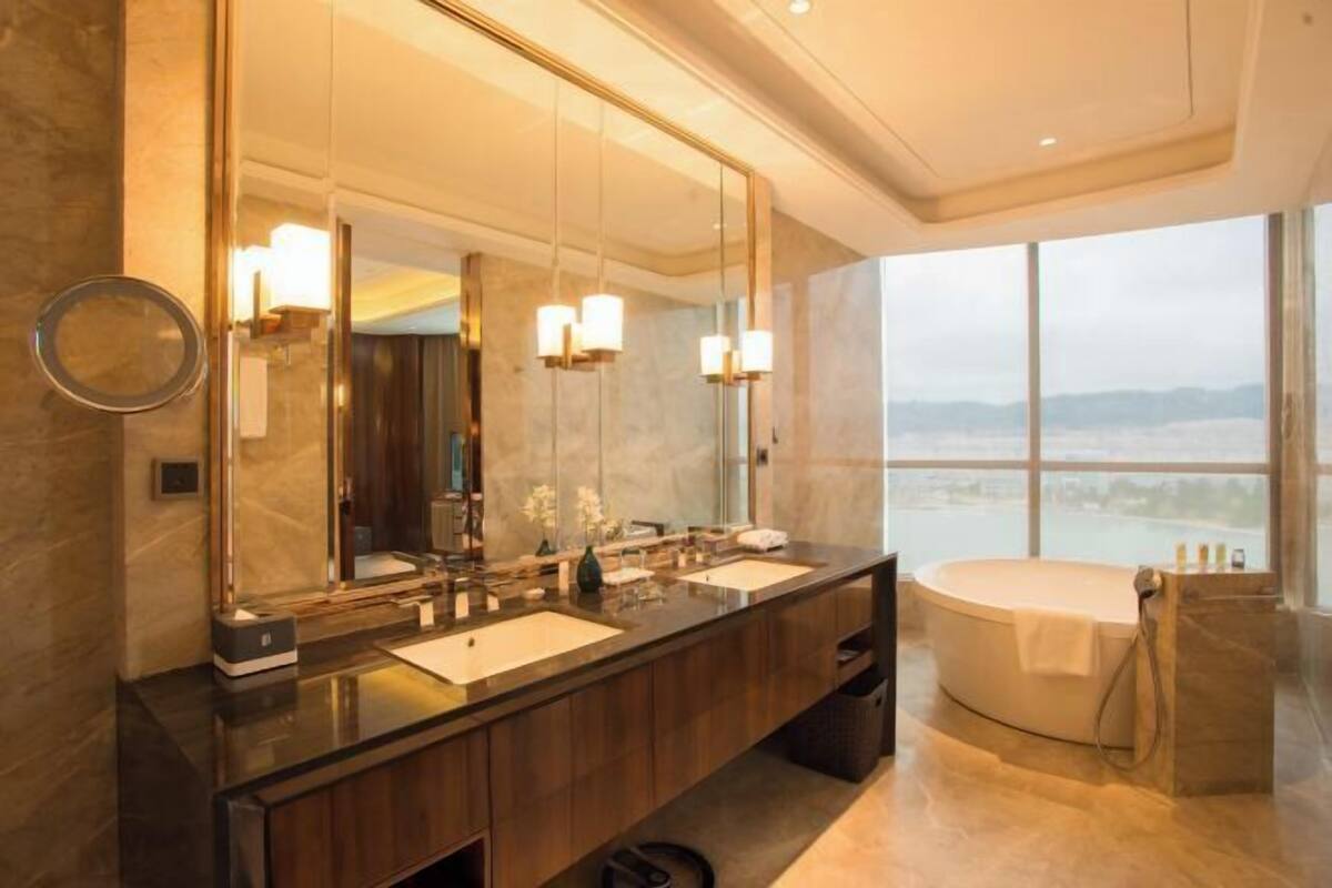 A modern bathroom with a large mirror, two sinks, a bathtub, and a view of the city.