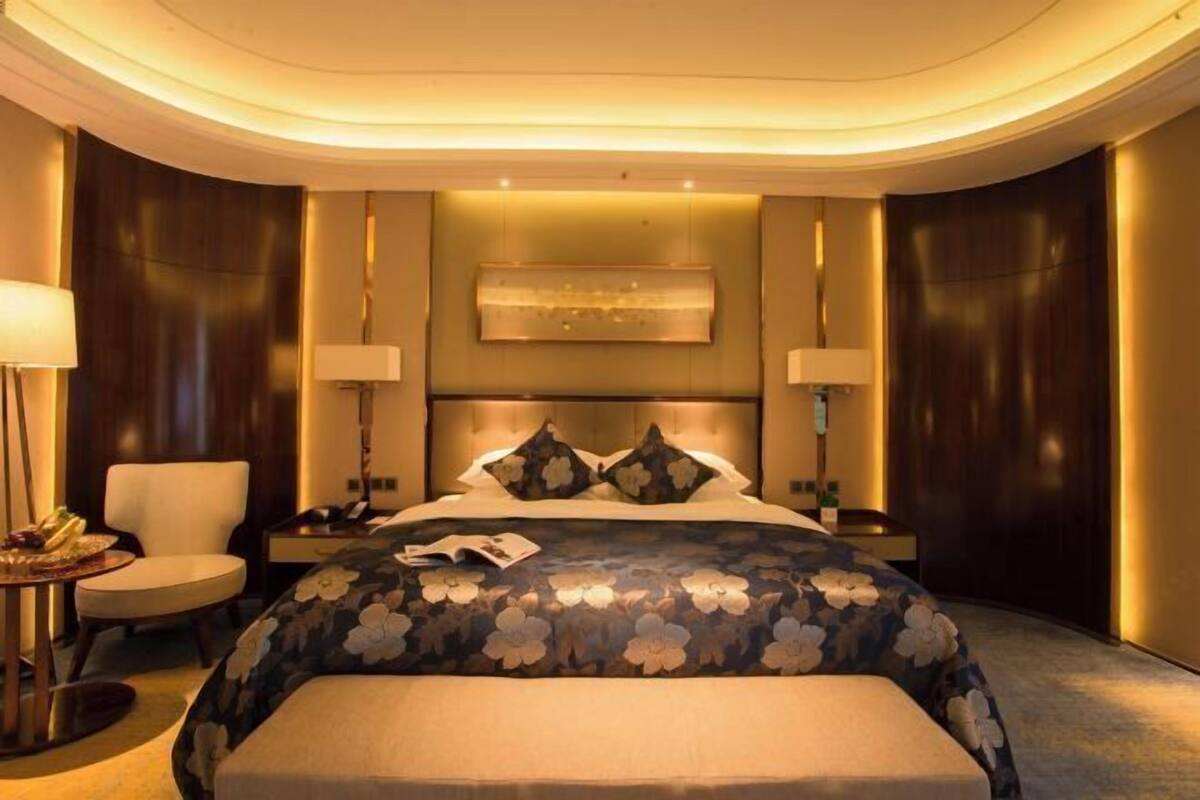 A hotel room with a large bed, bedside tables, a chair, and a round table with a lamp.